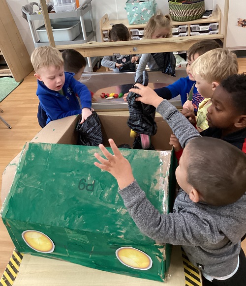 Children placing the pretend garbage they collected into the garbage truck their group created.