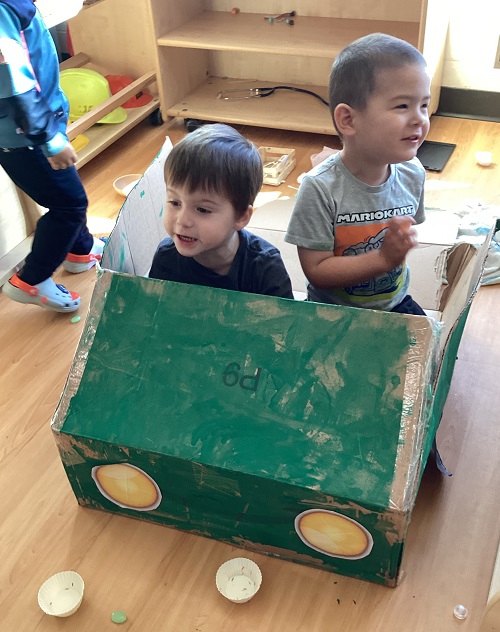 Two children engaging in imaginative play in the garbage truck their group created.