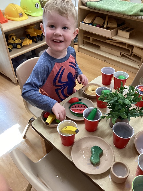 A child sitting at a table set-up with dramatic play food.