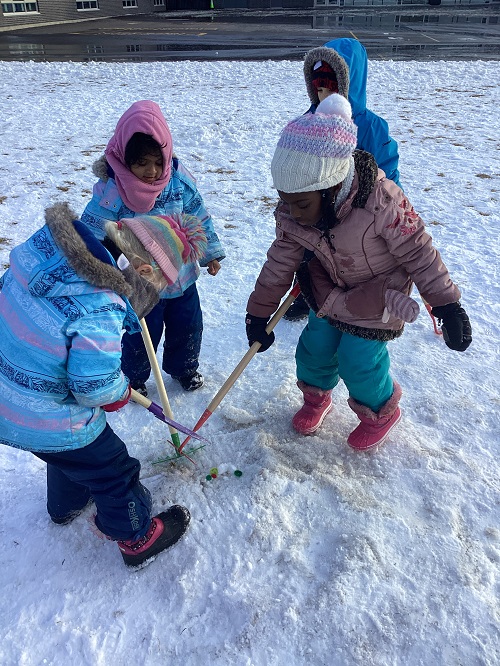 A small group of children using shovels to dig into the snow.