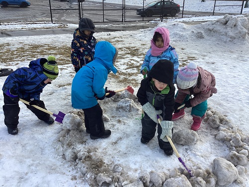 A group of children using shovels to dig and move the snow.
