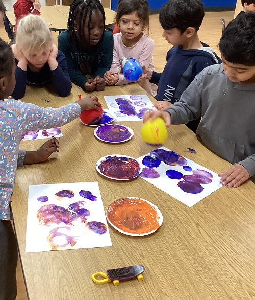 A small group of children painting with balloons.