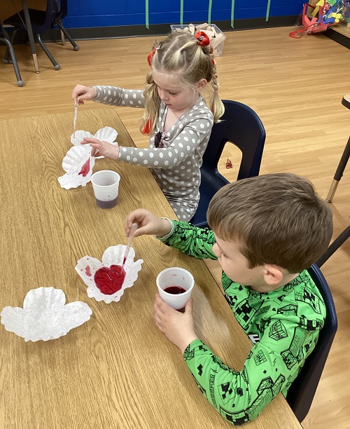 Two children using water droppers to colour the coffee-filter poppies red.