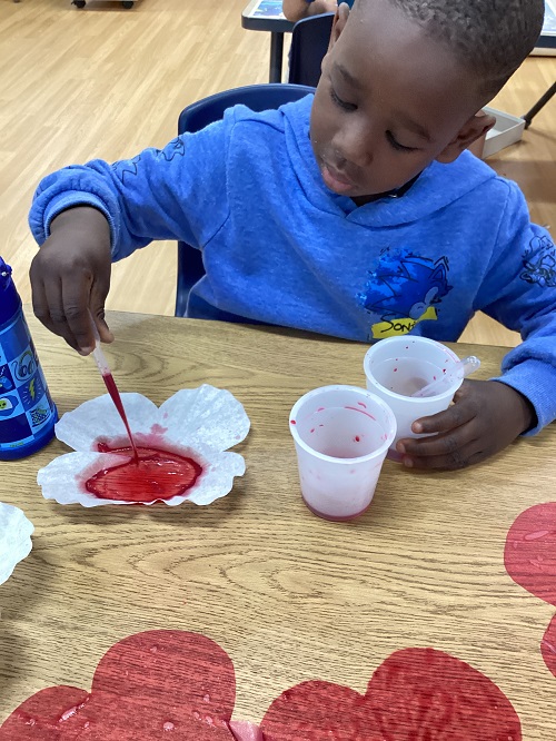 A child using a water dropper to colour a coffee-filter poppy red.