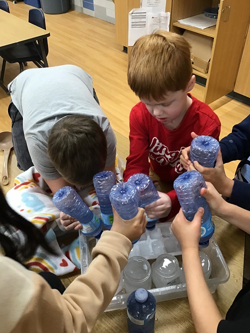 A small group of children squirting water into jars and ice trays.
