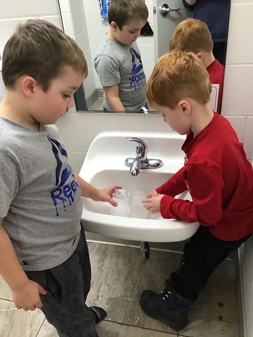 Two children filling jars with water at a sink.