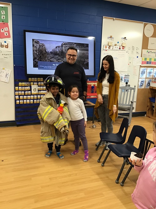 A firefighter, educator and child standing with another child wearing a firefighter uniform