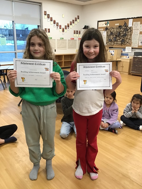 Two children holding up their reading certificates.