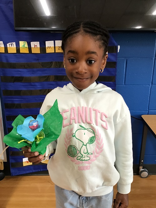 A child holding up a paper flower they made for their mother.
