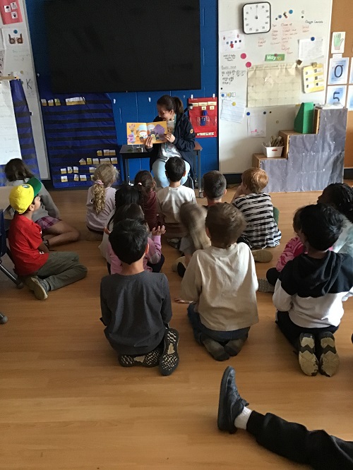 A group of children sitting with their educator, listening to a story.