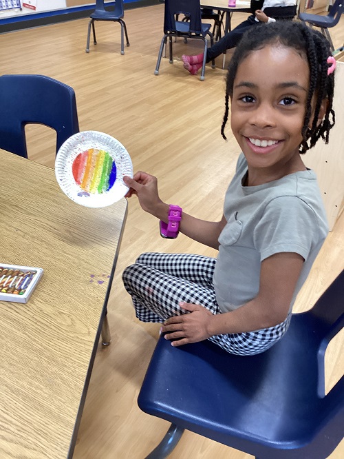A child holding up a rainbow painting.