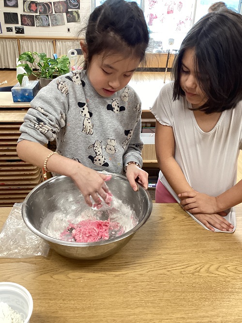 A child is mixing playdough in a bowl while a peer observes.