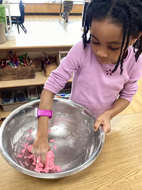A child mixing some pink playdough in a bowl.