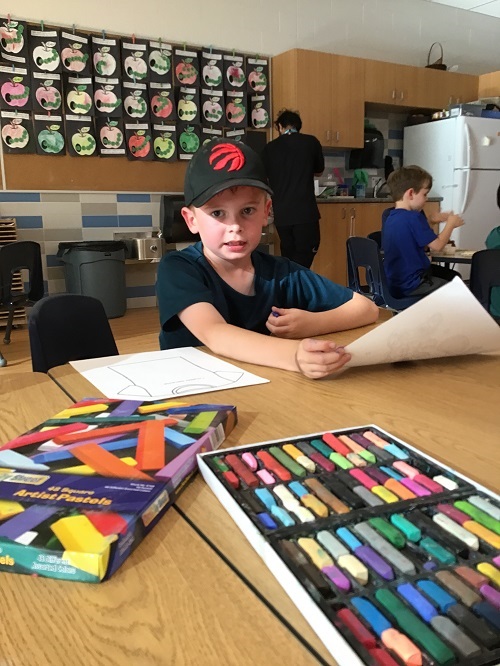 A school age child using pastels to colour an orange shirt 