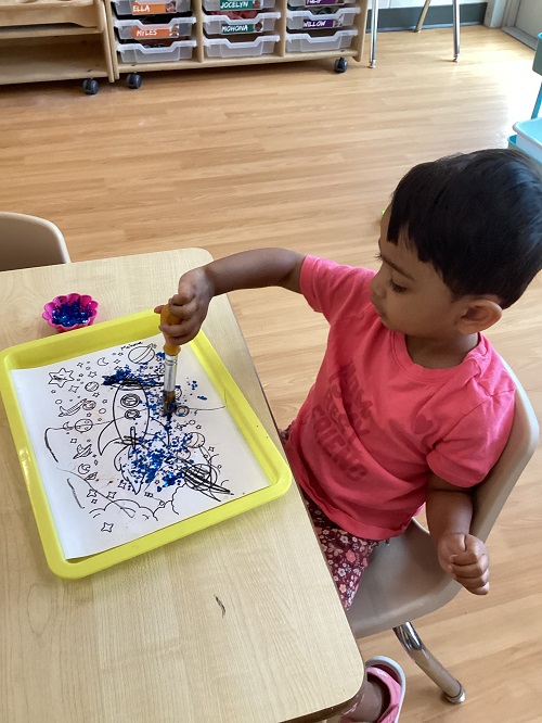 A child applying glitter to their picture.