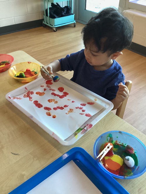 A child dabbing their pom-pom paintbrush onto paper