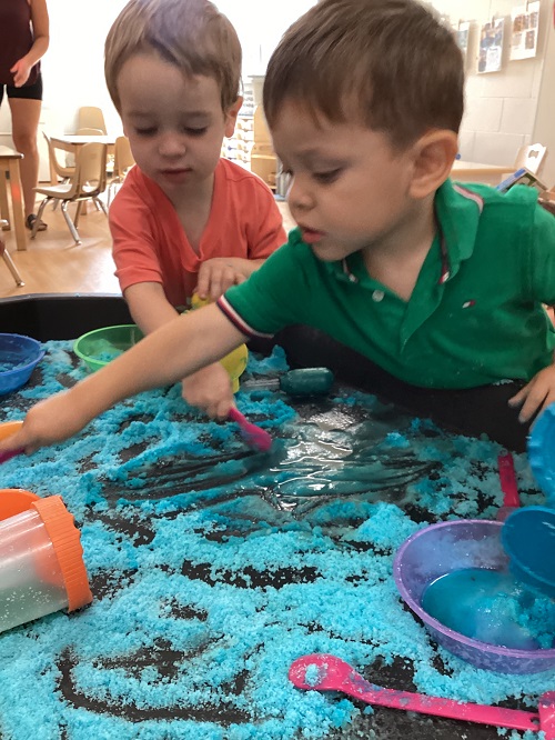Children using various materials to explore with coloured salt in a tuff tray.