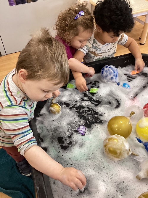 A small group of children exploring with foam and ice in the tuff tray.