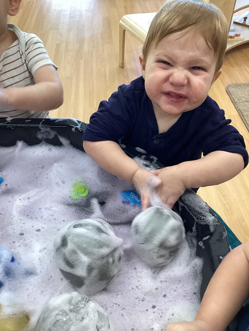 A child excitedly exploring with items in the tuff tray.