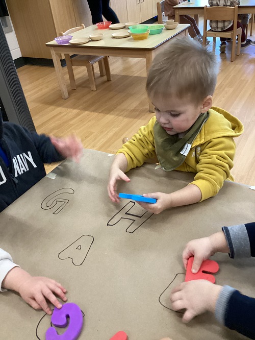 A child matching a foam letter to a drawn letter on the table