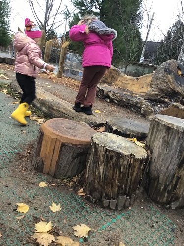 2 School Age children, one walking on a log and one standing beside them with their hand out