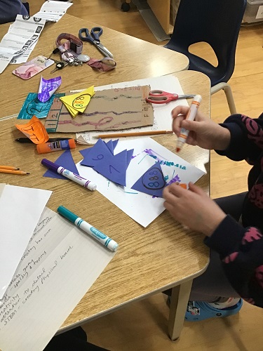 School Age 2 child sitting at the table with an orange marker colouring on a blue triangle with other triangles on the table in front of her