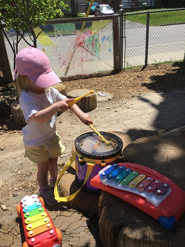 One child holding onto drum sticks and hitting the top of the drum with one stick, holding the other in the air