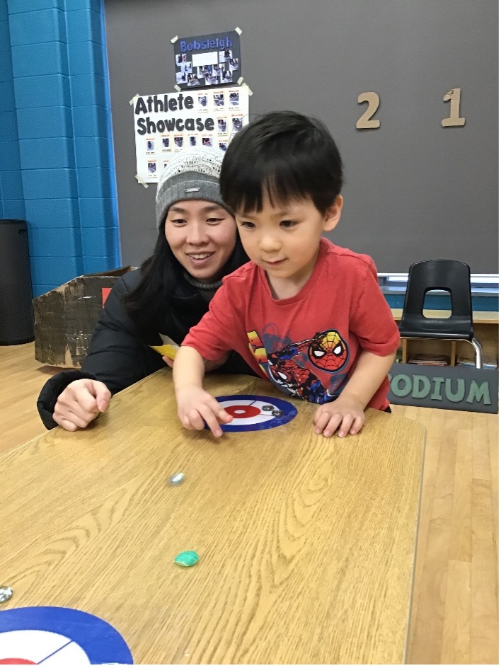 Child and parent play a game of curling in the classroom