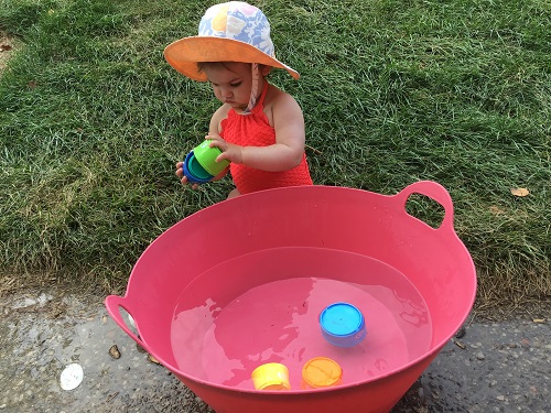 Child exploring a tub of water with toys