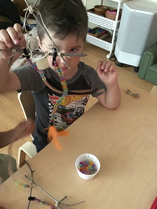 Child sitting at table holding up dream catcher with a small cup of beads on the table