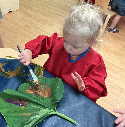 Child painting a giant leaf with a paint brush