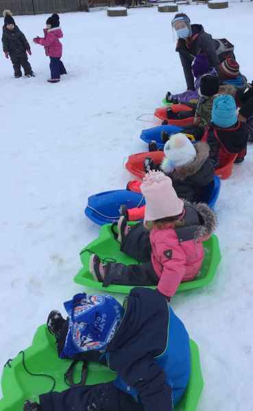 children lined up to slide down a snow covered hill