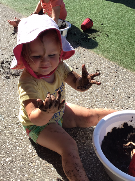 toddler girl playing outside getting her hands full of dirt