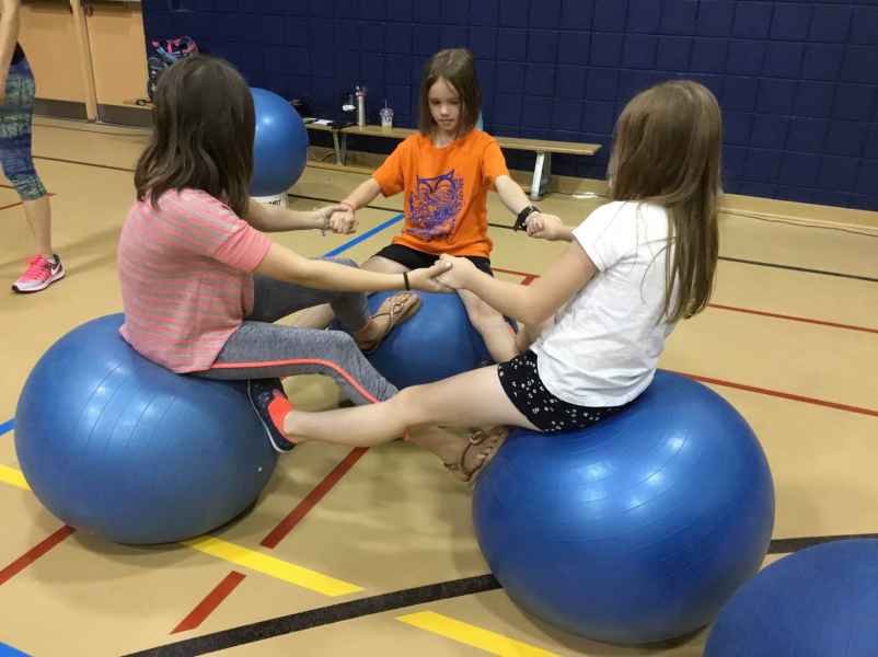 girls supporting each other as they balance on large stability balls