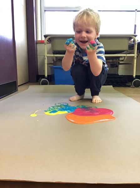 happy boy doing finger and feet painting on a large piece of paper
