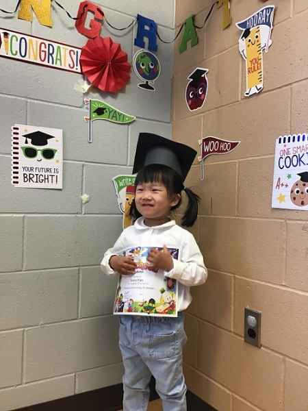 happy preschool graduate in a cap holding her certificate