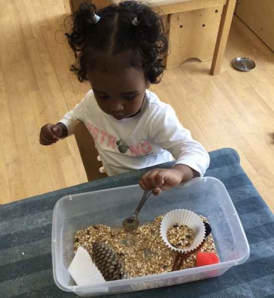 girl playing in a sensory bin with mixed items