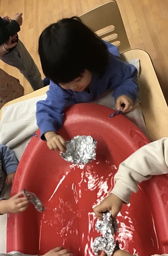 Preschool children have placed their homemade boats into water and are adding items to see if they will still float.