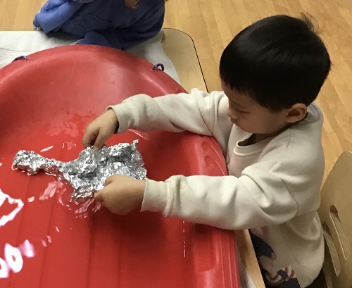 A preschooler is placing their tin foil boat into some water to see if it will float.