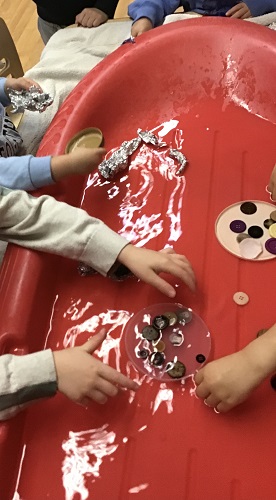 Several preschoolers have various materials in some water and are placing items in them to see if it floats.