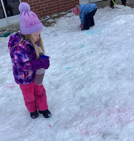 child holding a spray bottle filled with water and food colouring and spraying it on the snow