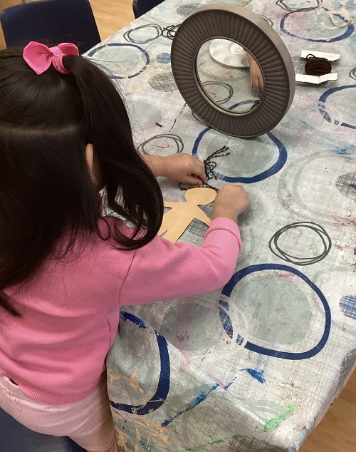 child sitting in front of a mirror and making a paper version of themself