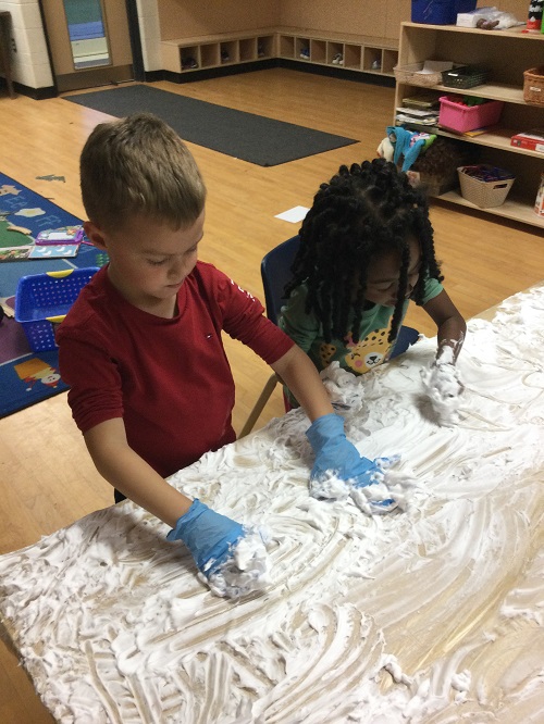 2 children, 1 child in gloves playing in shaving cream 