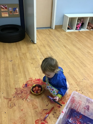 Girl sitting in the paint on the floor as she put all the balls into the red paint bowl