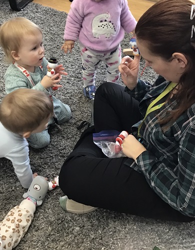 Several infants are playing with finger puppets with an educator.