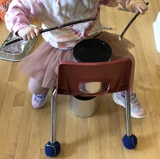 A preschooler is drumming with some stick on a coffee can.