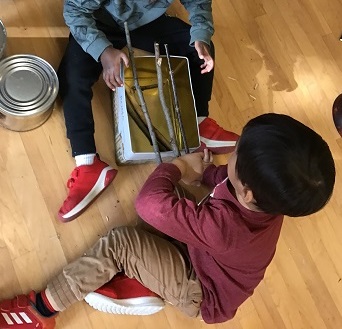 Two preschoolers have balanced sticks on top of a tin container.