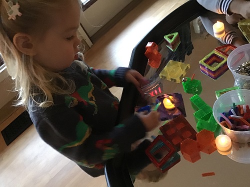 A preschooler is using magnetic tiles and tea lights to build on top of a mirror.