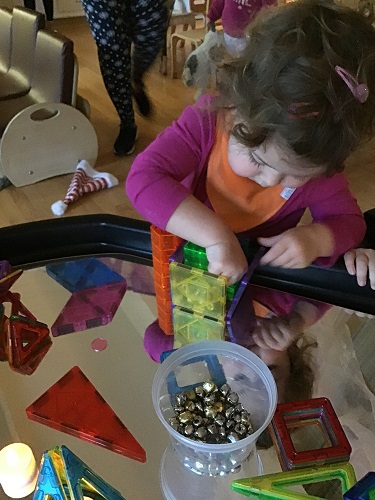 A preschooler is using magnetic tiles and tea lights to build on top of a mirror.