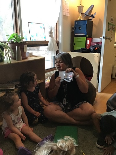 A preschool educator is sitting with a group of preschoolers showeing them a book.